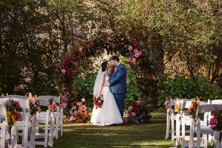 Newlyweds stand under a floral archway.